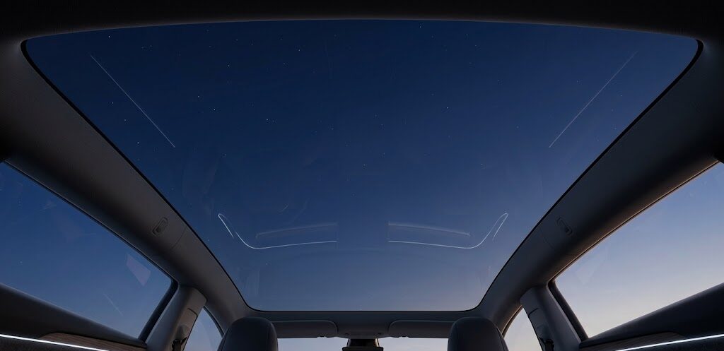Looking up through the fixed panoramic glass roof of a 2026 Tesla Model 3 Highland at a starry night sky.