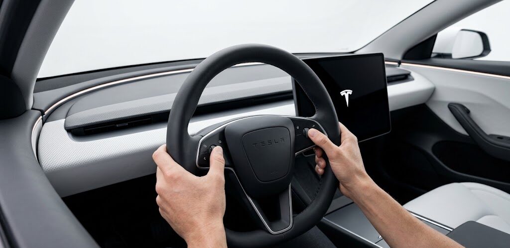 A driver performing a steering wheel scroll-wheel reset on a 2026 Tesla Model 3 Highland.